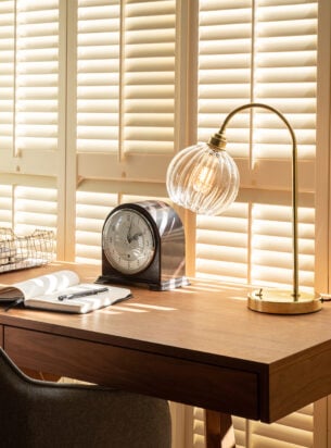 beautiful lamp featured on a stylish wooden desk with a clock and notepad, a great example of including designer table lamps in your lighting scheme .