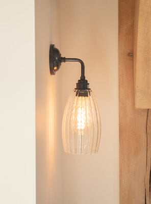 Upton wall light from Fritz Fryer Lighting with ribbed glass shade and bronze fixings. This simple wall light can be wired to shine the light up or down your wall. Here it is featured pointing down in a hallway with an oak beam