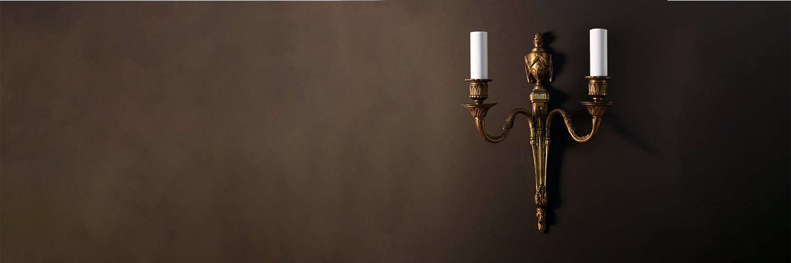 Beautiful antique wall light with gadrooned detail, gilt metal finish and two arms set against a dark background