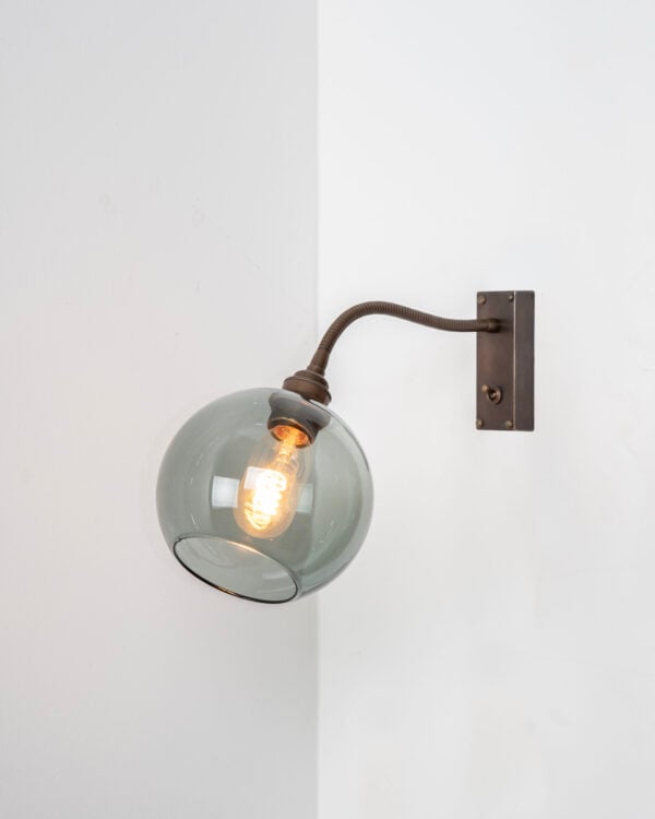 Antique Brass metal finish flexible wall light installed on white wall, featuring smoked glass Hereford glass shade