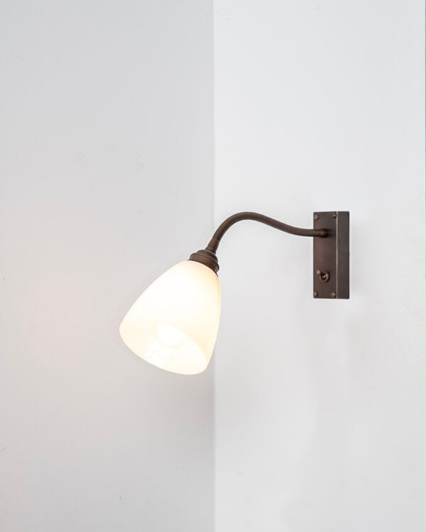 Antique Brass metal finish flexible wall light installed on white wall, featuring white glass Pixley glass shade