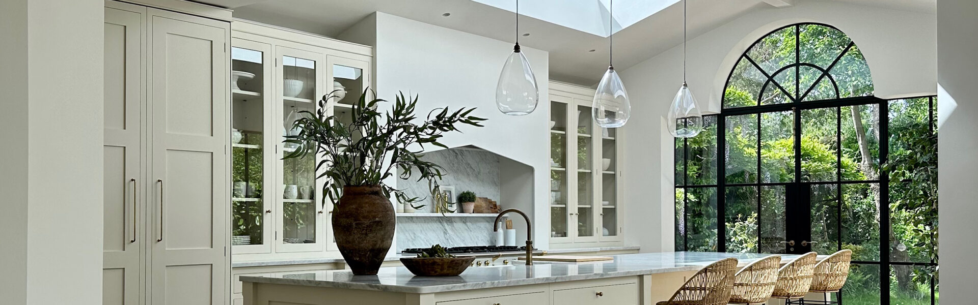 White kitchen with large central island, illuminated by three Fritz Fryer clear glass pendant lights hanging from the ceiling, enhancing the ambiance.