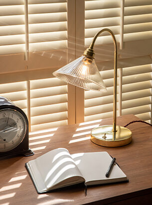 Home office desk with diary and clock, illuminated by a contemporary table lamp in a polished brass metal finish.