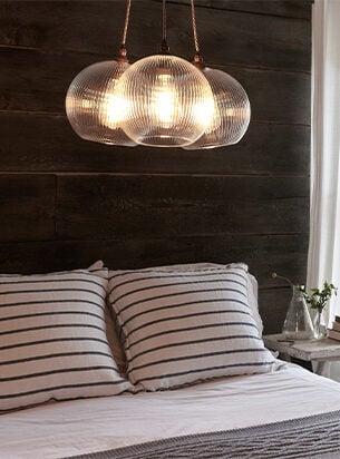 A 3 globe cluster pendant light hung over a bed with a wooden headboard and stripey pillows