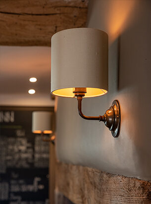 Hotel wall lights on a grey background with fabric shades and antique brass metalwork shown from the side