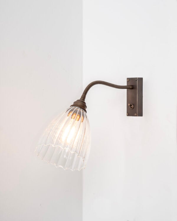 Antique Brass metal finish flexible wall light installed on white wall, featuring ribbed glass Ledbury glass shade