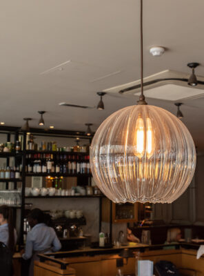Large globe pendant ight in ribbed glass at the front of this commerial project with a bar in the background