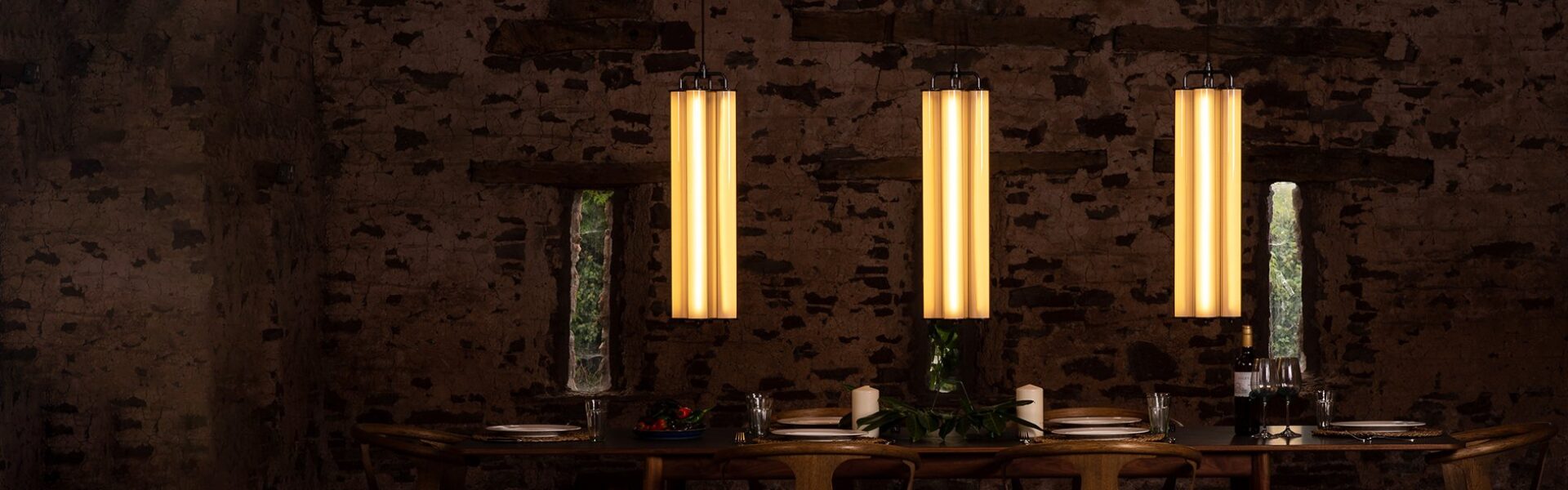 Fritz Fryer Pendant Lights hung in a row over a large dinning table. The pendants each feature 4 light tubes held together with brass fixtures