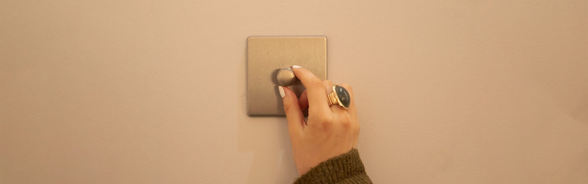 Dimmable light switch on a white wall being dimmed to control the dimmable lighting within the room.