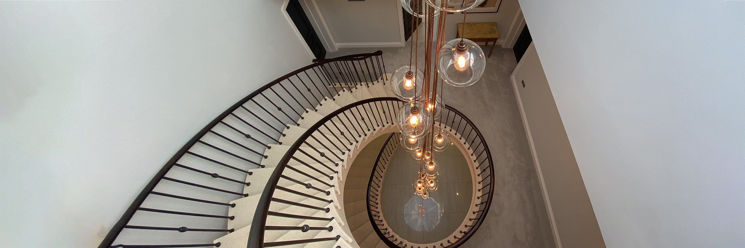 Spiral stairway adorned with cluster of clear globe lights, ideal stairwell lighting ideas for residential or commercial stairwells.