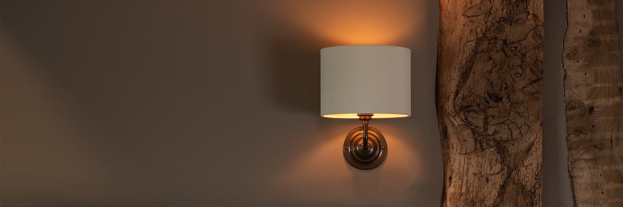 The Classic wall light with Fawley fabric shade in an antique brass finish, beside old beam in hotel.