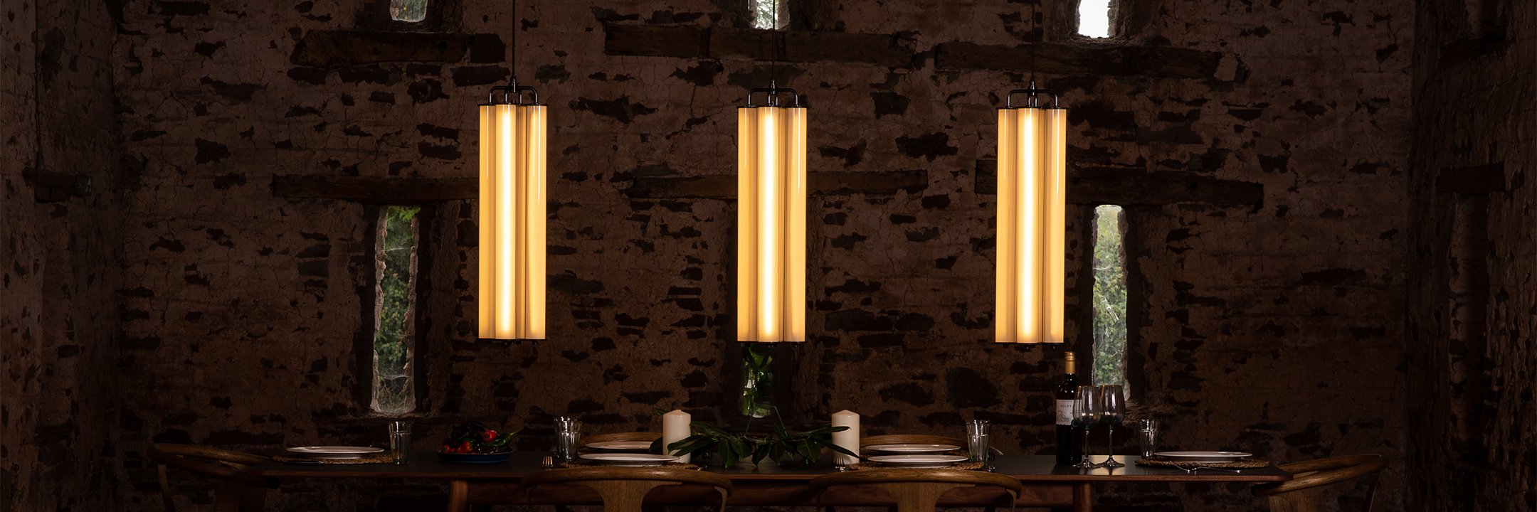 Three pillar lights from the Alton lighting collection, hung in a row over a large dining table.